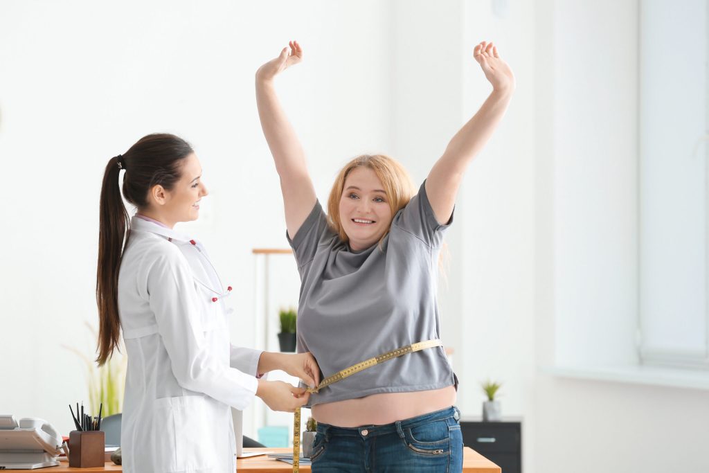Young female doctor measuring waist of overweight woman with cen